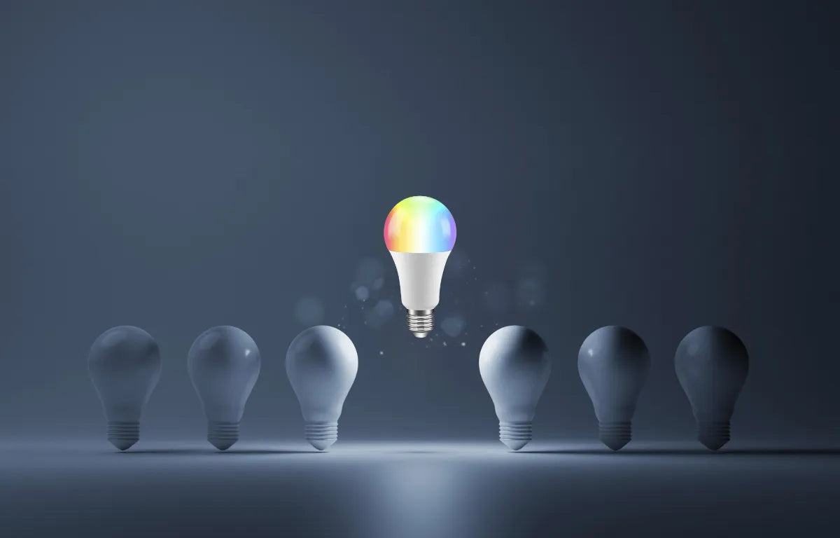 Six Regular Light Bulbs Standing on Floor with a single Multi Color Light Bulb Elevated Above Them